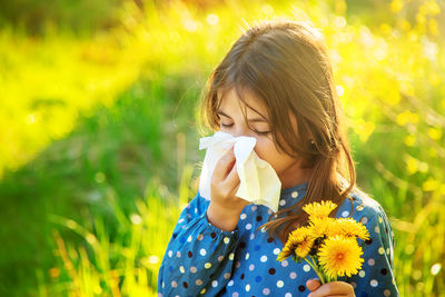 Girl holding flower blowing nose with tissue