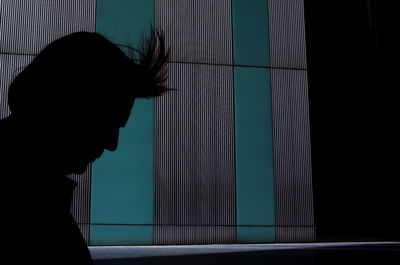 Portrait of silhouette woman with wind in hair standing against wall 