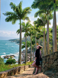 Young woman standing by palm trees against sky