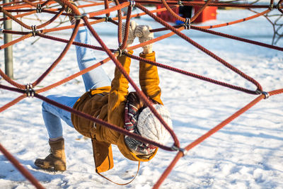 Full length of woman climbing on ropes at snow covered park