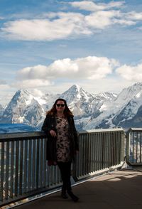 Portrait of woman standing with snowcapped mountain in background against cloudy sky