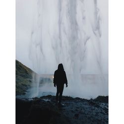 Rear view of man standing by waterfall