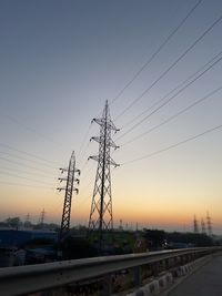 Electricity pylons against clear sky during sunset