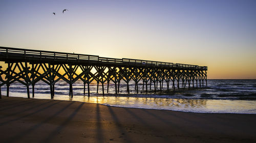 Pier on beach against sky during sunset