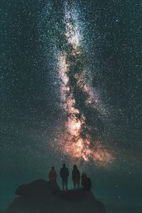 Low angle view of silhouette friends on mountain against star field