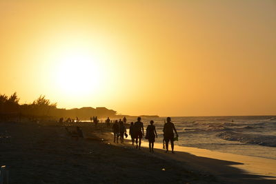 Group of people walking on beach at sunset