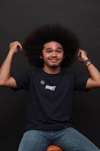 Man with black frizzy hair, black short shirt, jeans and black background, photo in studio