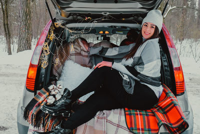 Brunette woman wrapped in blanket in trunk car. travel in winter. car decorated with festive 