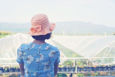 Rear view of woman standing against greenhouse and sky