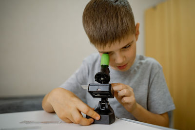 Boy 7 years old, at home in the room looks through microscope