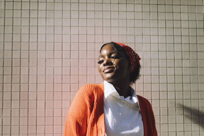 Portrait of young woman standing against wall