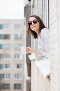 Young woman wearing sunglasses standing against built structure