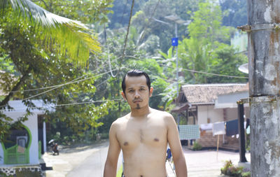 Portrait of shirtless man standing against trees