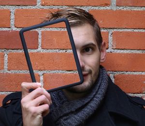 Young man holding mirror with reflection of brick wall