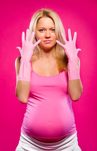 Portrait of pregnant woman exercising standing against pink background