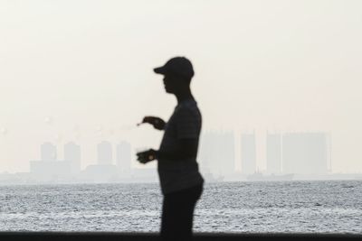 Silhouette man standing by sea against sky during sunset