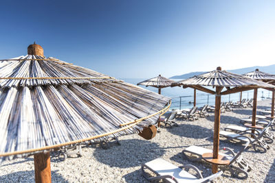 Thatched roofs at beach against blue sky on sunny day