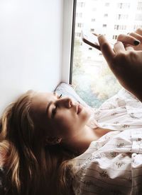 High angle view of woman using mobile phone while lying in alcove window seat