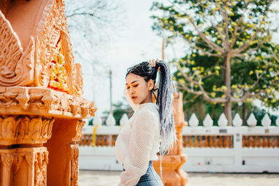 Woman looking away while standing against built structure