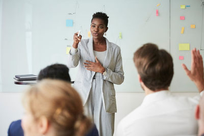 Businesswoman pointing while young colleague with hand raised sitting in office seminar at workplace