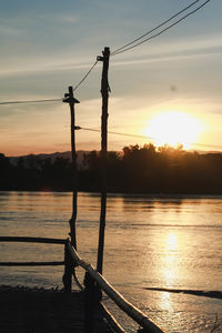 Silhouette man standing by lake against sky during sunset