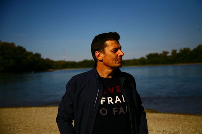 Man standing by lake against blue sky