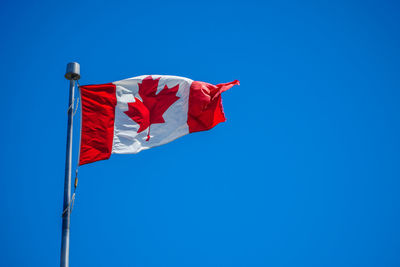 Low angle view of canadian flag waving against blue sky