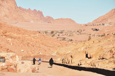 People walking on desert against clear sky