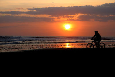 Silhouette man riding bicycle at beach against sky during sunset