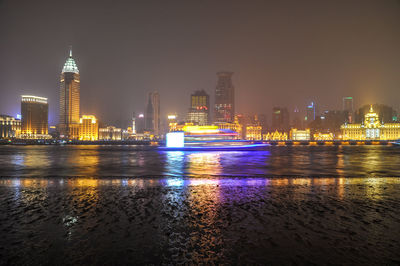 Illuminated buildings by river against sky in city at night