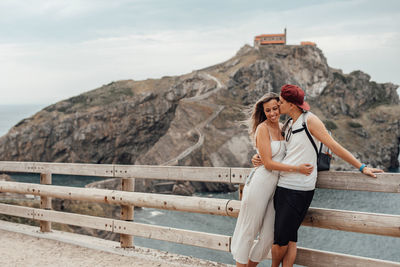 Couple embracing while standing by railing against sea