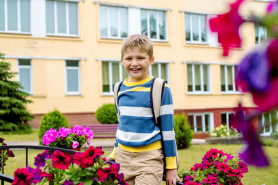 Portrait of boy standing on footbridge by flower against school building