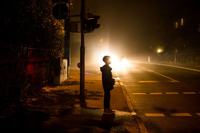 Boy standing on illuminated street at night