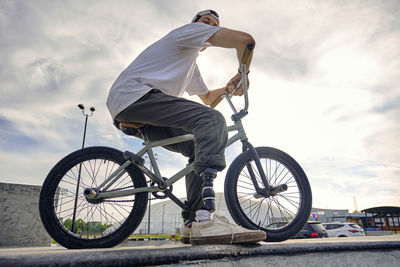 Bmx rider with prosthetic foot confidently posing on bike against cloudy sky at skateboard park