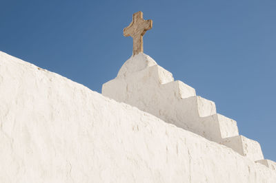 Close-up of a white roof exterior of a church with a stone cross, greece, cyclades islands, mykonos.