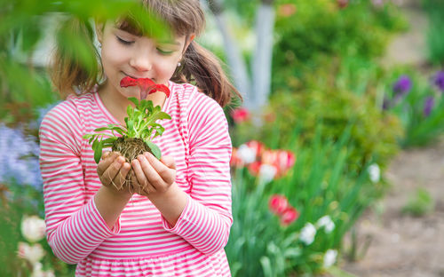 Smiling girl holding flower plant in hands cupped