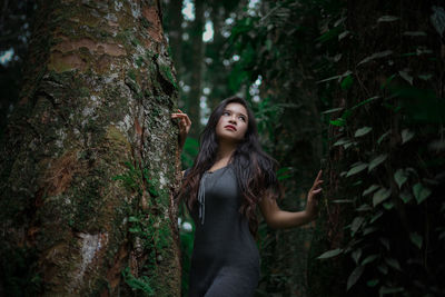 Young woman standing by tree trunk in forest