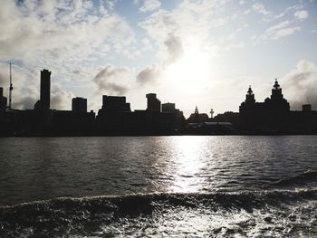 Silhouette buildings by river against sky during sunset