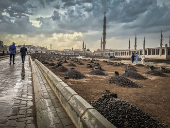 Rear view of people walking by concrete on under construction road against cloudy sky