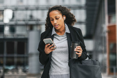 Businesswoman using smart phone while holding insulated drink container