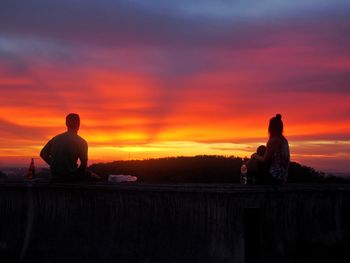 Silhouette men sitting on shore against sky during sunset