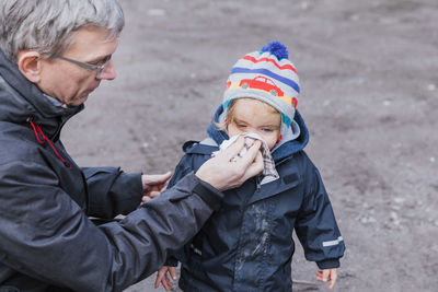Grandfather cleaning nose of granddaughter on road