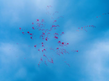 Low angle view of colored balloons flying against blue sky