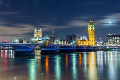 Westminster bridge over thames river by illuminated big ben and city at night