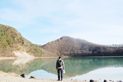 Rear view of man standing on mountain by lake