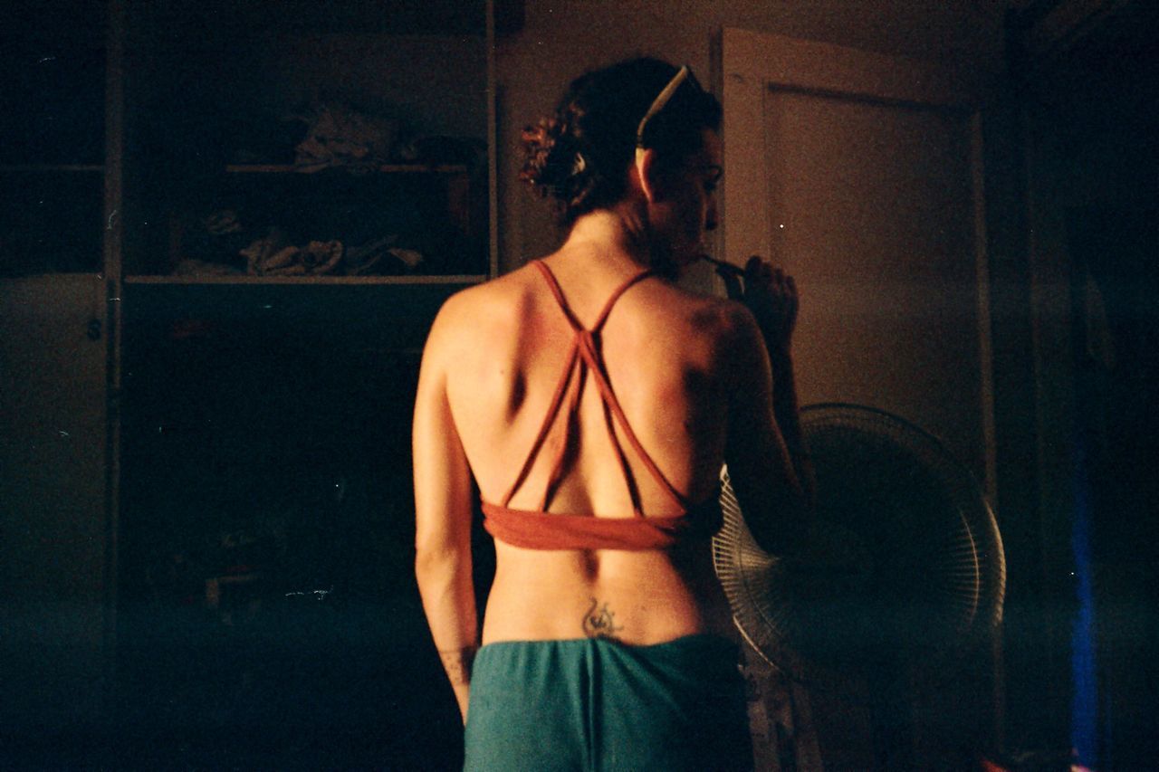 REAR VIEW OF SHIRTLESS WOMAN STANDING AGAINST CURTAIN