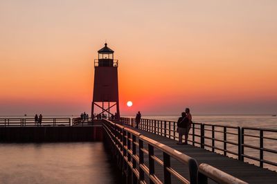 People on pier over sea against sky during sunset