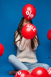 Low section of woman with red balloon standing against blue background