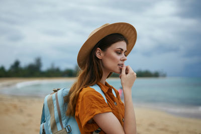 Portrait of beautiful young woman looking away at beach against sky