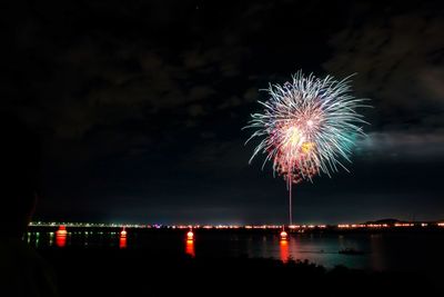 Firework display over river against sky at night